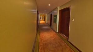 Een hotelhal met tapijtvloeren, houten deuren en een groen bord aan de muur.