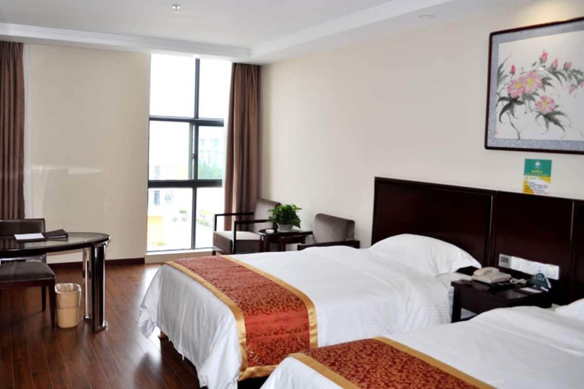 A hotel room with two beds, a desk, a chair, and a window with curtains.