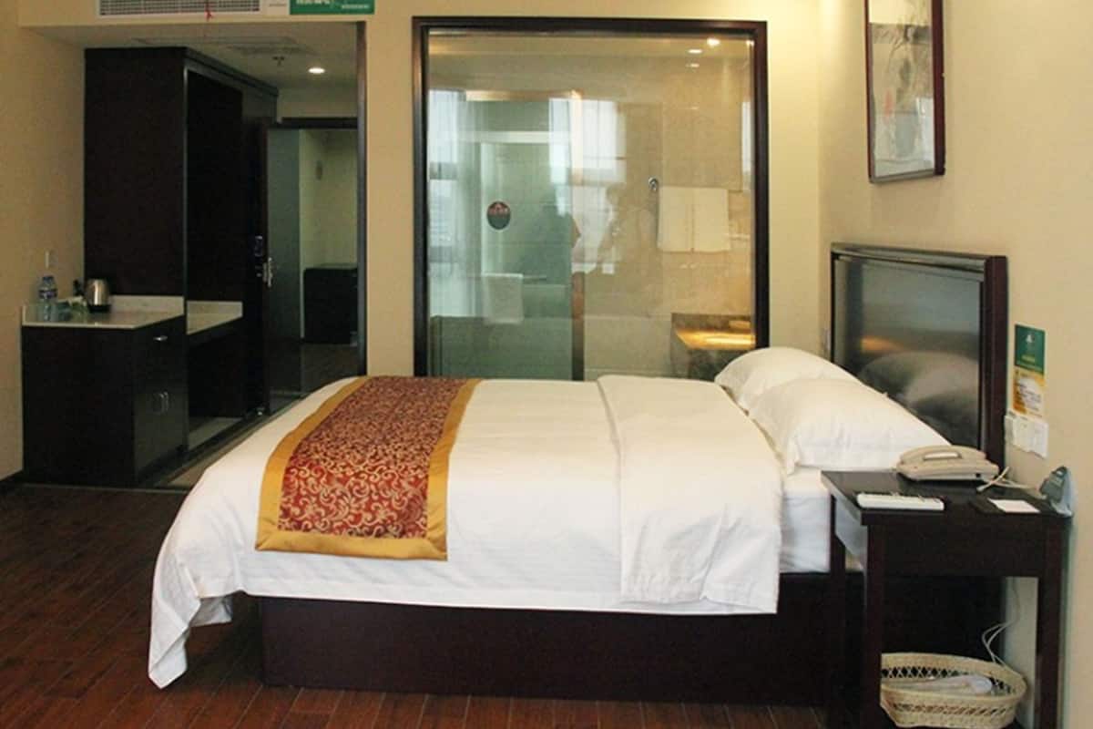 A hotel room with a bed, bedside table, and a mirror.