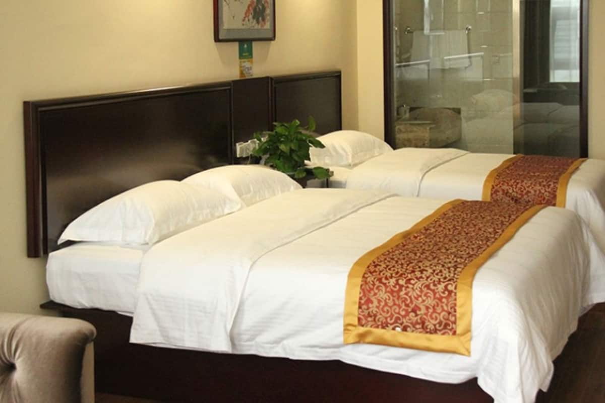 A hotel room with two beds, a dark headboard, a plant, and a glass shower area.