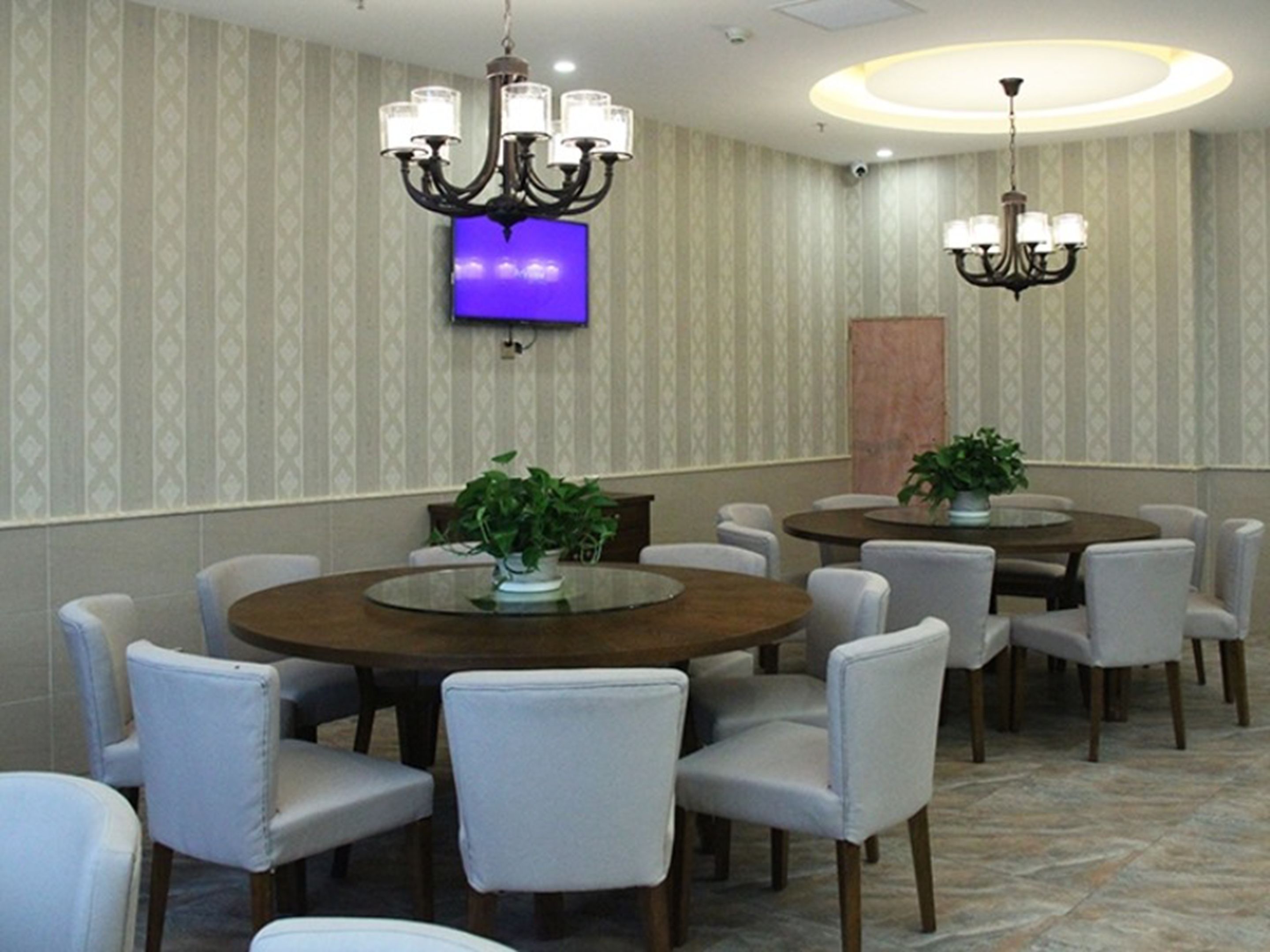 A conference room with round tables and chairs, a chandelier, a television, and patterned wallpaper.