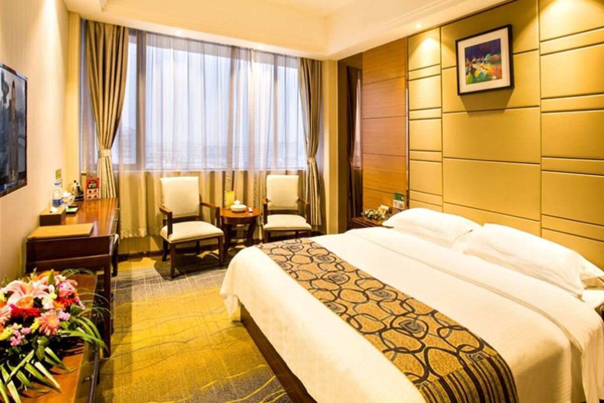 A hotel room with a large bed, two chairs, a desk, and a window with curtains.