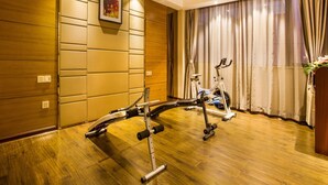 A room with a wooden floor, a stationary bike, and a wall-mounted exercise machine. - GreenTree Inn JieYang Bus Terminal Station RongHua Avenue Hotel (Jieyang)