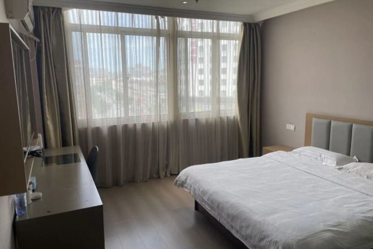 A hotel room with a bed, a desk, and a window with curtains.