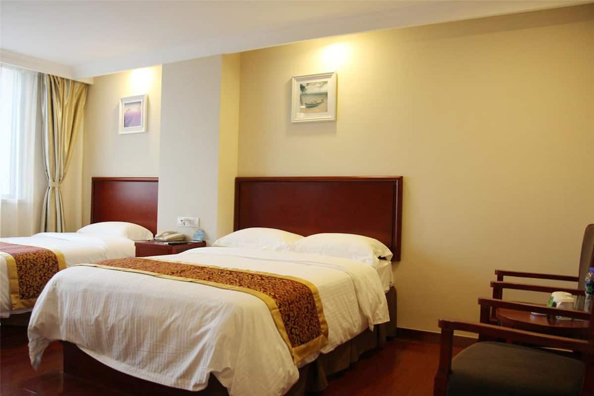 A hotel room with two beds, a wooden headboard, a chair, and a nightstand with a phone.