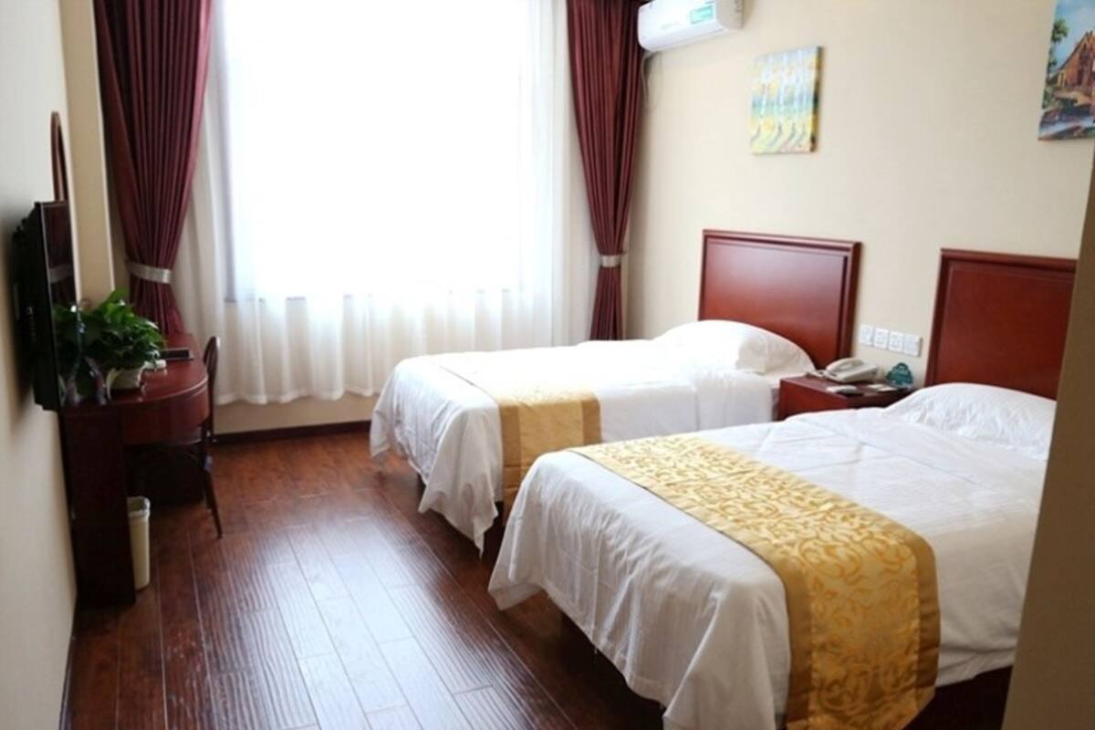 Ett hotellrum med två sängar, ett trägolv, ett skrivbord med en stol, en växt och en tavla på väggen.