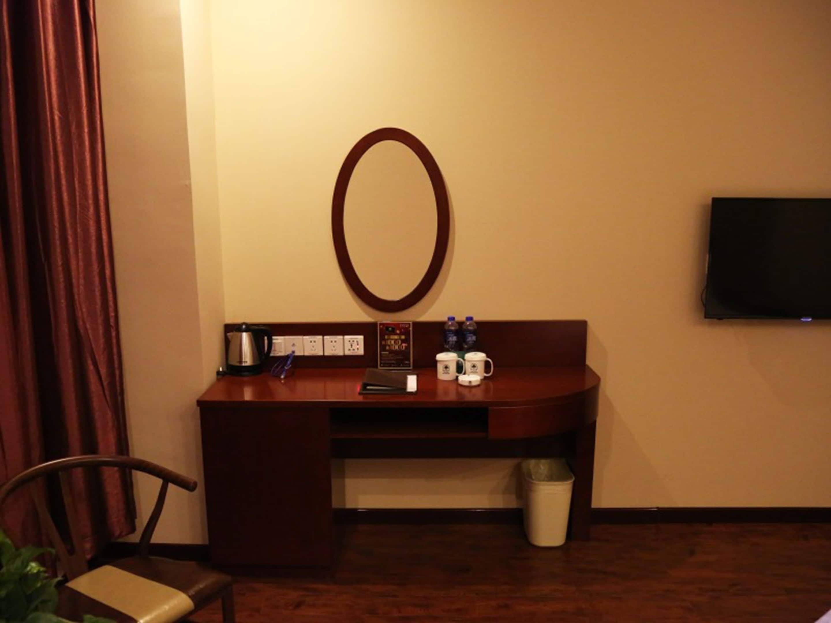 A hotel room with a wooden desk, a television mounted on the wall, and a small trash bin.