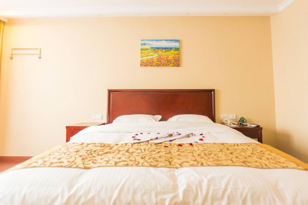 Un lit bien fait, avec une couvre-lit à motifs, une tête de lit en bois et un tableau représentant un paysage accroché au mur.