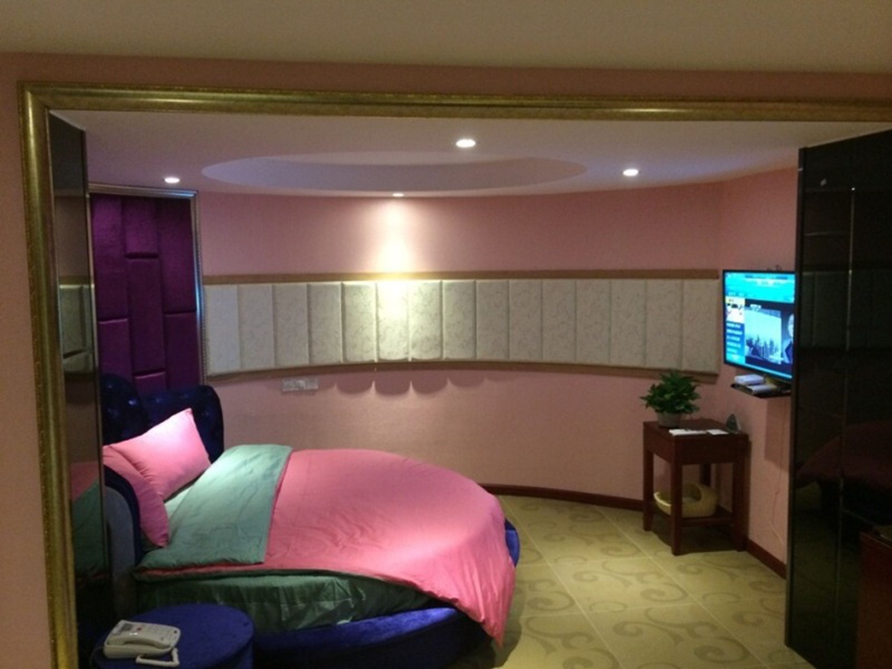 A hotel room with a curved bed, a television, a small table, and a mirror.