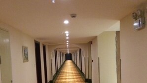 Un largo y estrecho pasillo de hotel con alfombra estampada, puertas a ambos lados y luces empotradas en el techo.