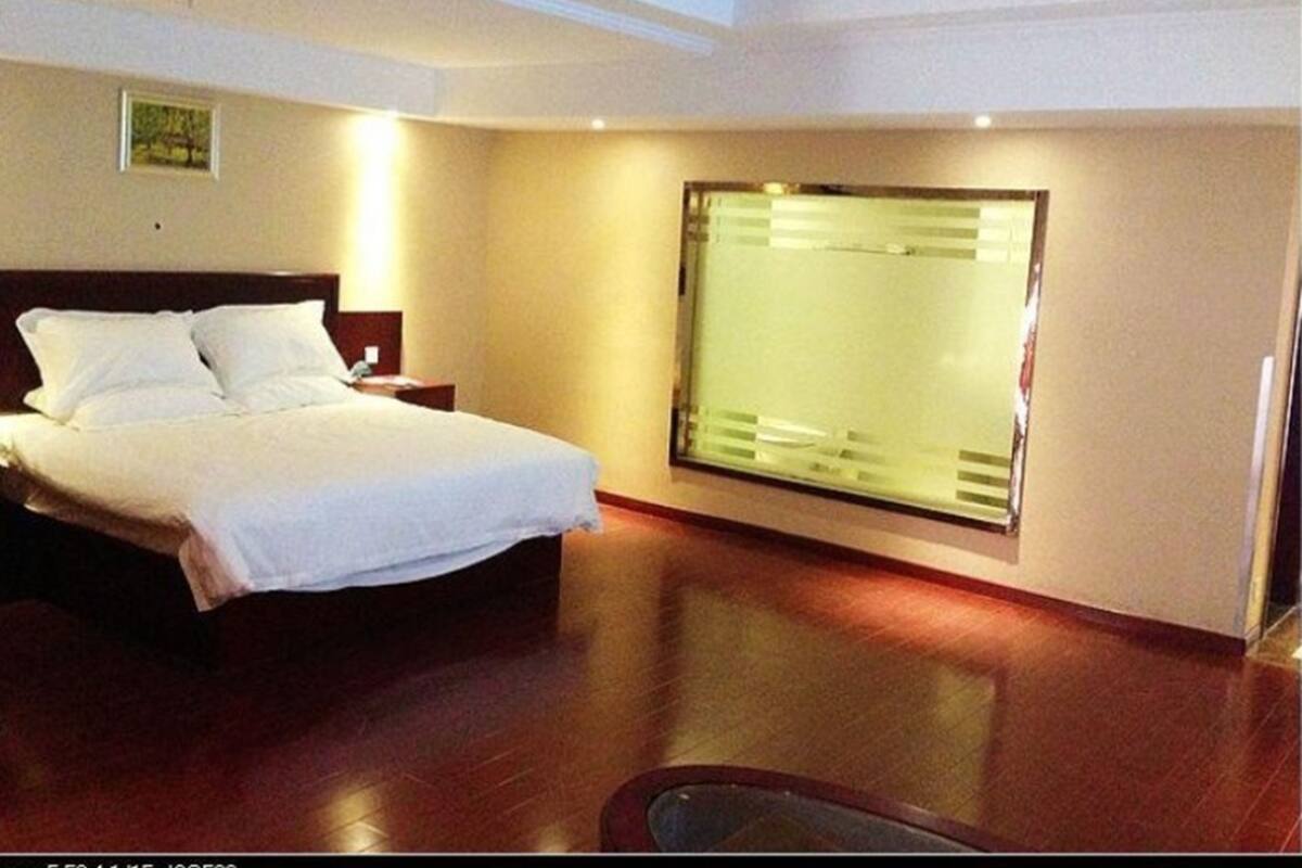 Een hotelkamer met een bed, een nachtkastje, een raam met jaloezieën en een houten vloer.