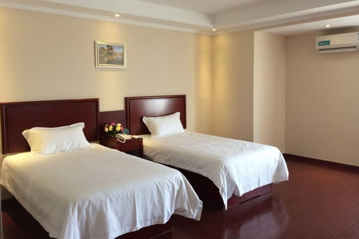 Een hotelkamer met twee eenpersoonsbedden, een nachtkastje met telefoon en bloemen, een schilderij aan de muur en een airconditioning.