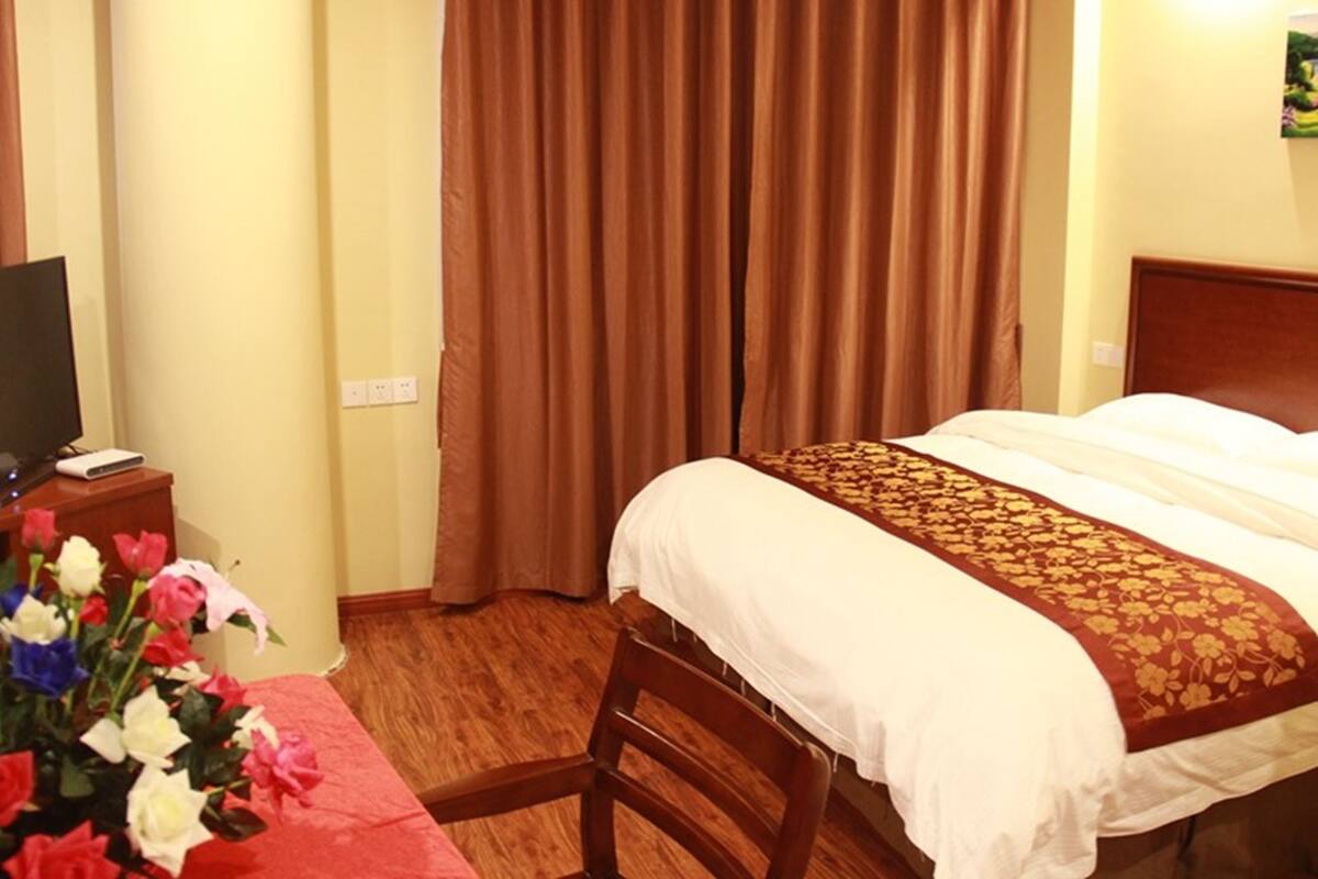 Une chambre d’hôtel avec un lit, un téléviseur posé sur une table en bois et un arrangement floral.