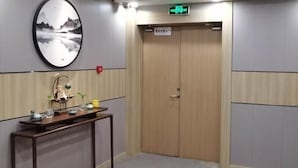 Habitación de hotel con puerta de madera, un cuadro colgado en la pared, una mesita con objetos decorativos y un cartel que indica una salida.