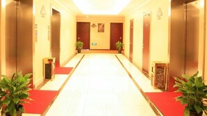 A hotel corridor with a red carpet, doors on both sides, and potted plants at the end of the corridor. - GreenTree Inn Shaoxing Keqiao Xingyue Road Zhongqing Building Hotel (Shaoxing)