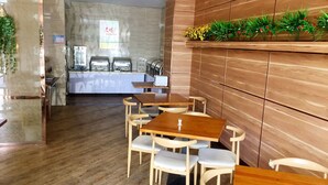 A modern restaurant interior with wooden tables and chairs, a kitchen area in the background, and a decorative plant shelf. - GreenTree Inn Yancheng Economic Development Zone Management Committee Express Hotel (Yancheng)
