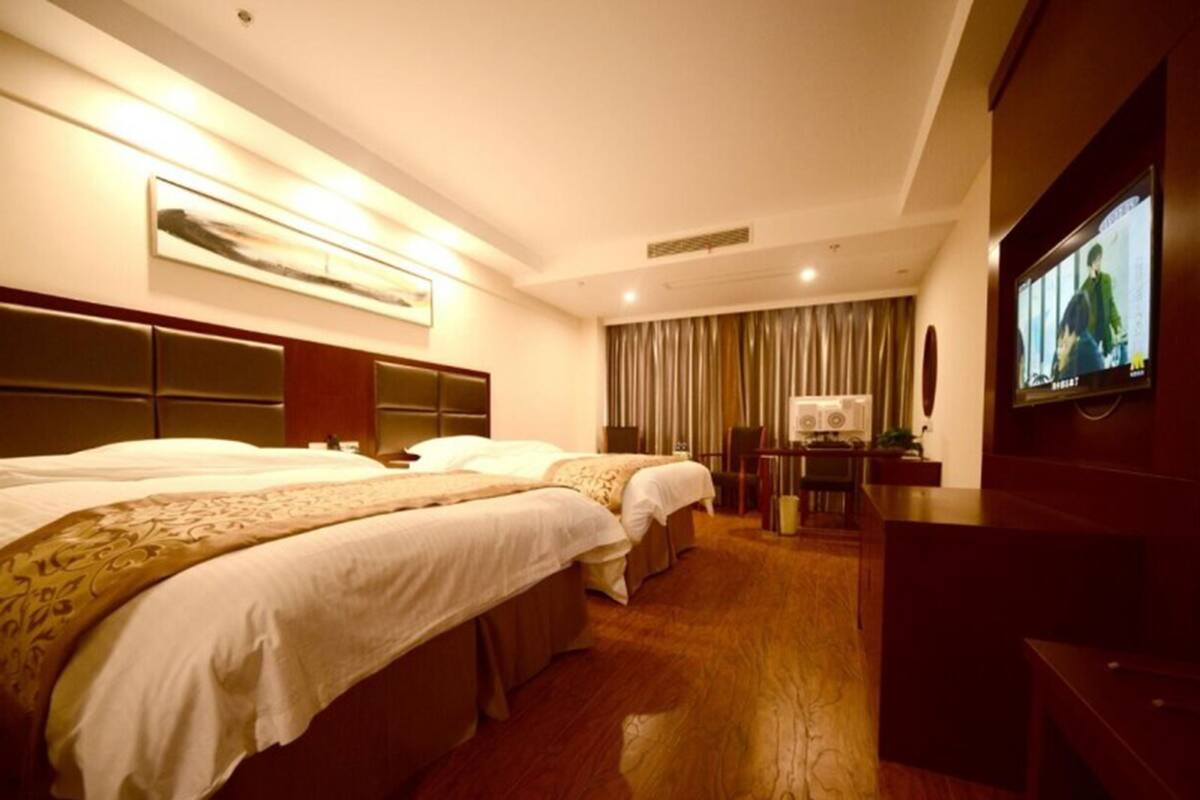 Ein Hotelzimmer mit zwei Betten, einem Schreibtisch, einem Fernseher und einem großen Fenster mit Vorhängen.