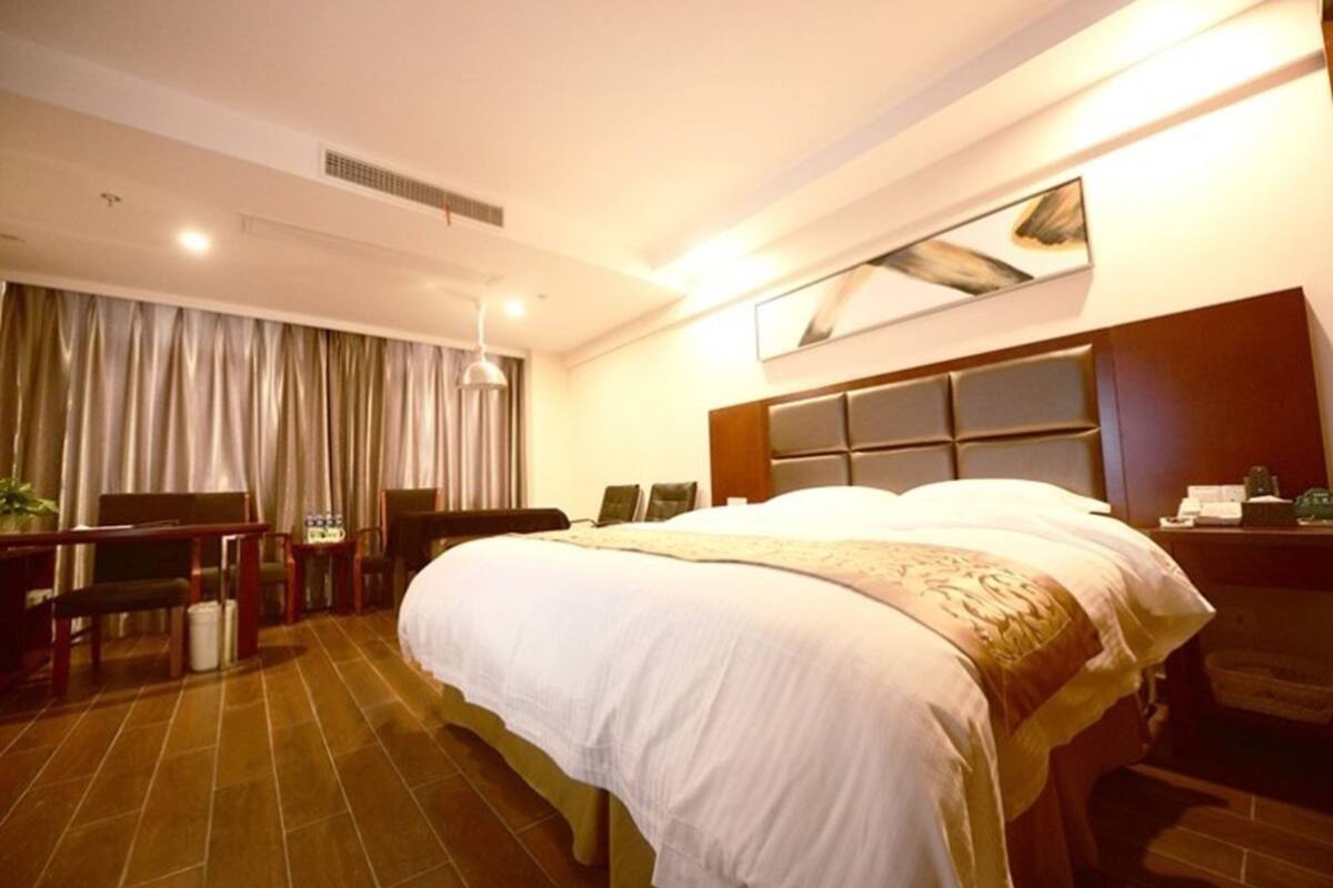 Ein Hotelzimmer mit einem großen Bett, einem Schreibtisch mit Stuhl, einem Fernseher und einem Fenster mit Vorhängen.