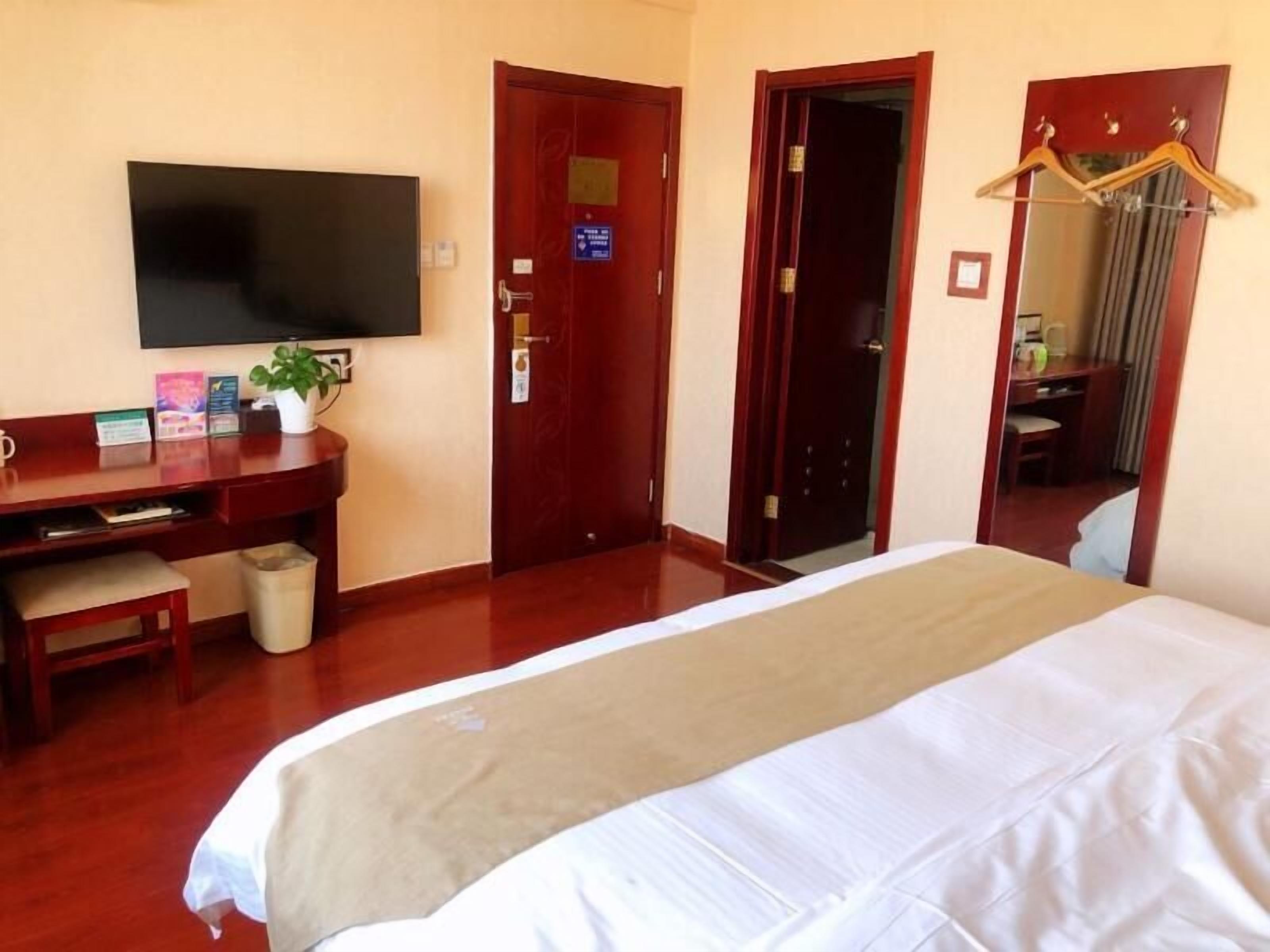 A hotel room with a bed, desk, chair, television, and a mirror.