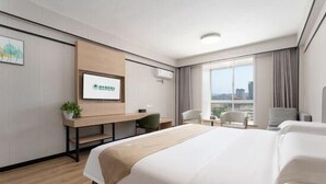 A modern hotel room with a large bed, a desk, a chair, and a view of the city through the window. - Greentree Inn Weihai Wendeng Darunfa Business (Weihai)