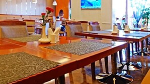 Ein Hotel-Speisesaal mit langen Holztischen, gepolsterten Sitzgelegenheiten und dekorativen Vasen.