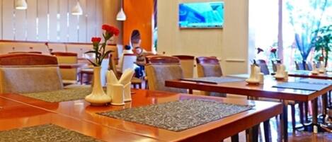 A hotel dining area with long wooden tables, cushioned seating, and decorative vases.