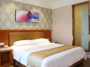 Una habitación de hotel con cama, mesita de noche, un cuadro en la pared y una puerta.