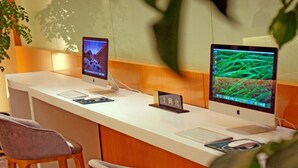Ein Empfangsschalter mit zwei Monitoren, einer Tastatur und einer Maus. Zwei Stühle und ein kleiner Tisch mit einem Schild stehen daneben.