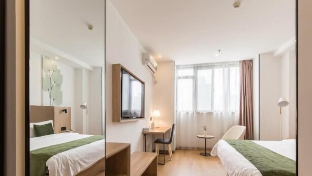 Habitación de hotel con dos camas, un escritorio, una silla, un televisor y una ventana con cortinas.