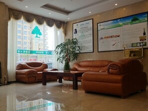 A lobby with leather sofas, a coffee table, and a large plant. There are informational posters on the walls and a view of a building outside.