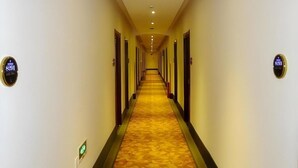 Un pasillo de hotel con suelo alfombrado, puertas a ambos lados y un reloj digital en la pared.