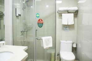 Une salle de bain avec une douche à parois de verre, des toilettes et un lavabo. Des serviettes sont suspendues sur un porte-serviettes et un distributeur de savon est fixé au mur.
