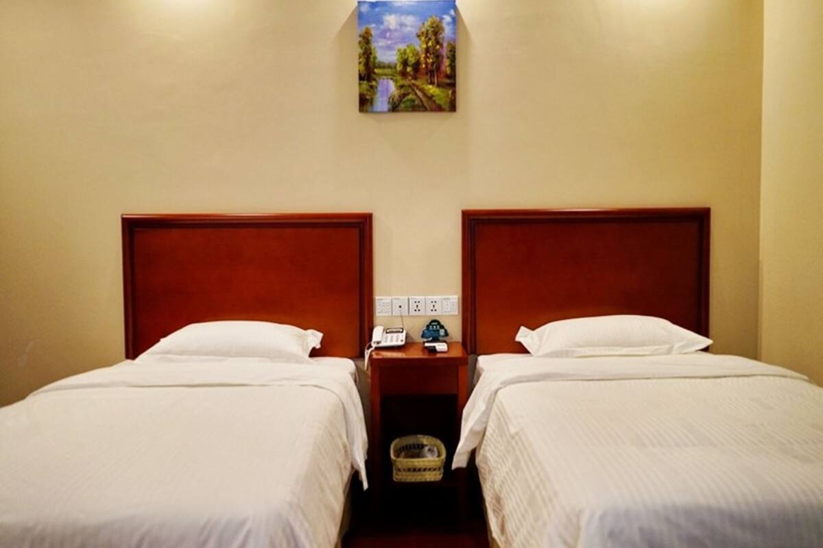 Et hotelværelse med to enkeltsenge, trægavle, hvide sengetøj, et natbord med en lampe, en telefon og et billede af et landskab.