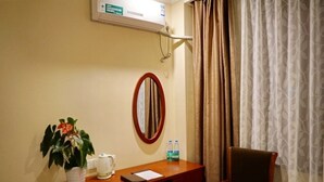 Una habitación de hotel con escritorio, silla, planta en maceta, hervidor de agua, botellas de agua y espejo.