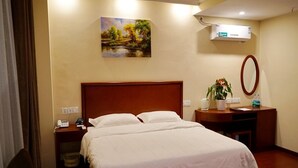 Habitación de hotel con una cama grande, una mesita de noche con teléfono y lámpara, un escritorio pequeño con espejo, y un cuadro en la pared.