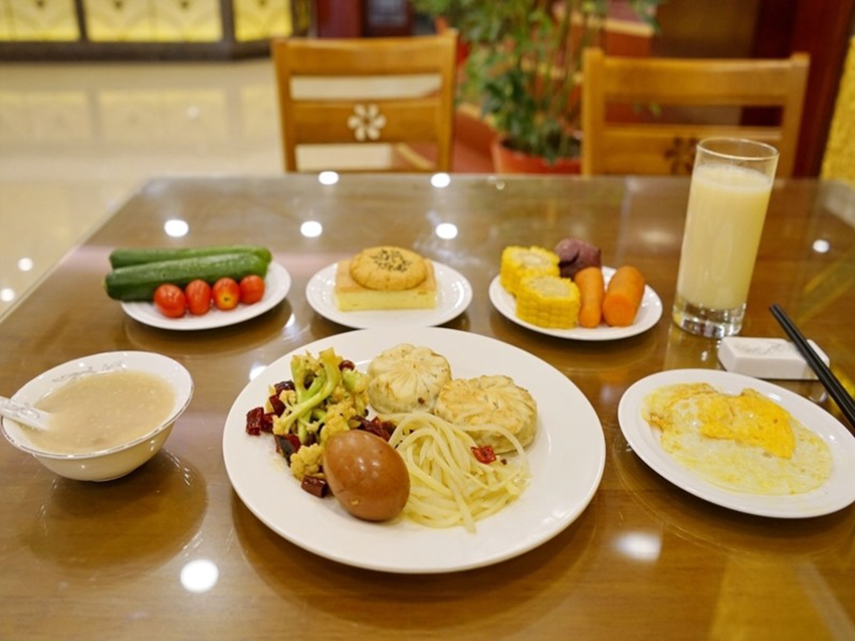 A dining table with plates of food, a glass of milk, and a bowl of soup.