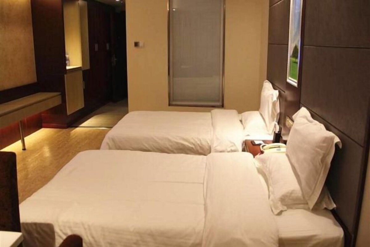 Camera d'albergo con due letti, pavimento in legno, un'ampia finestra e televisore a parete.