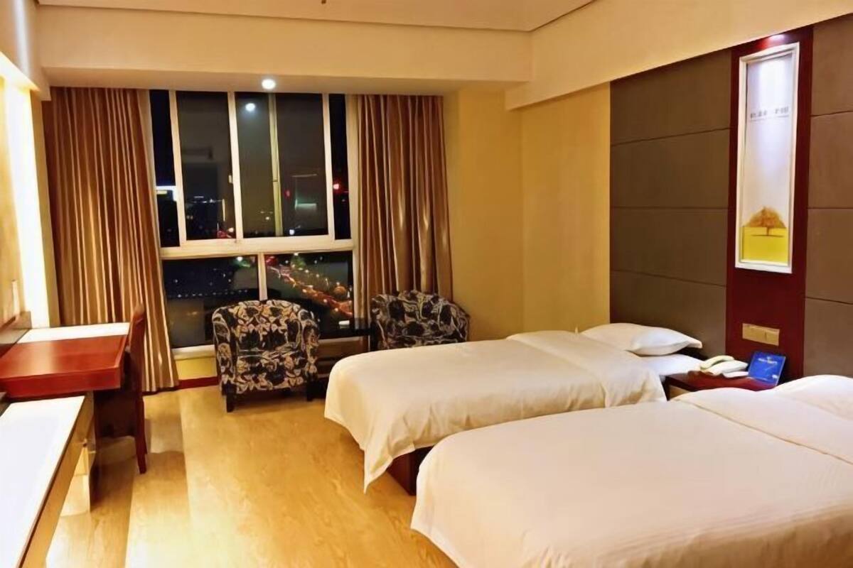 Ett hotellrum med två sängar, ett skrivbord, en stol och utsikt över en stadssiluett i nattljus.