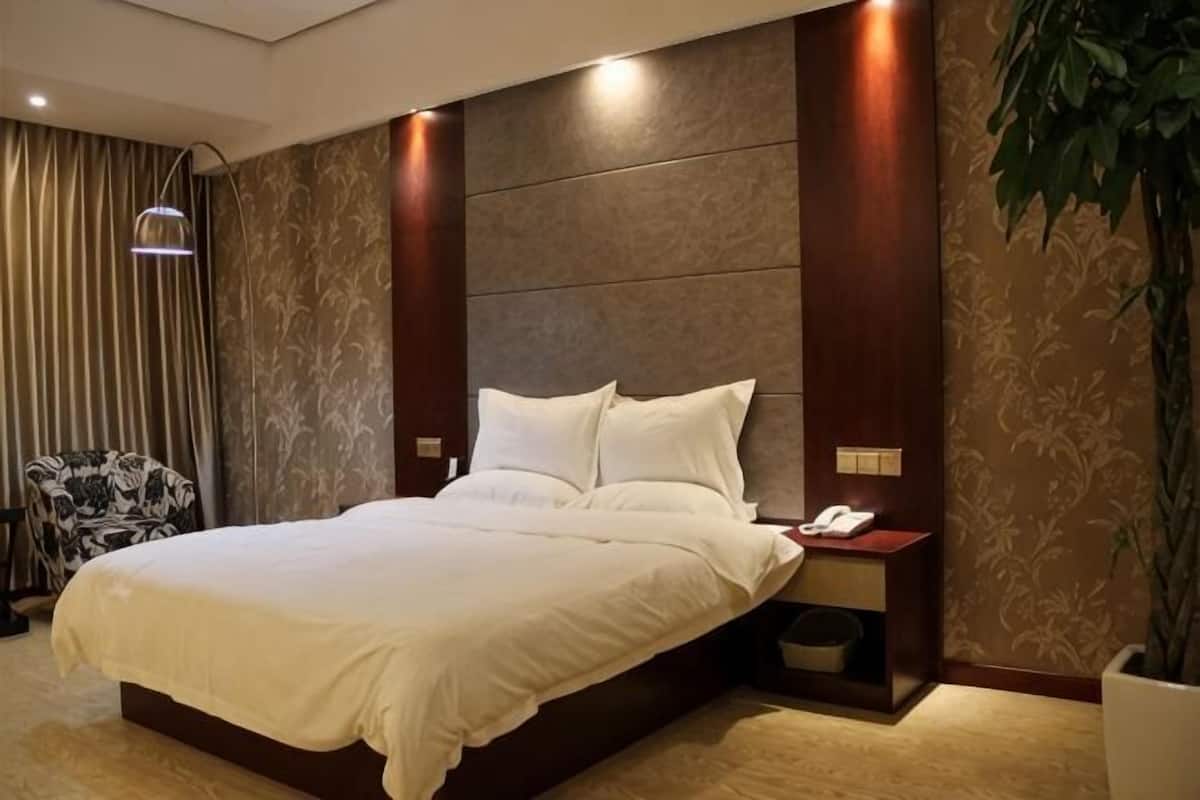A neatly made bed with white linens, a bedside table with a phone, and a wall-mounted lamp.