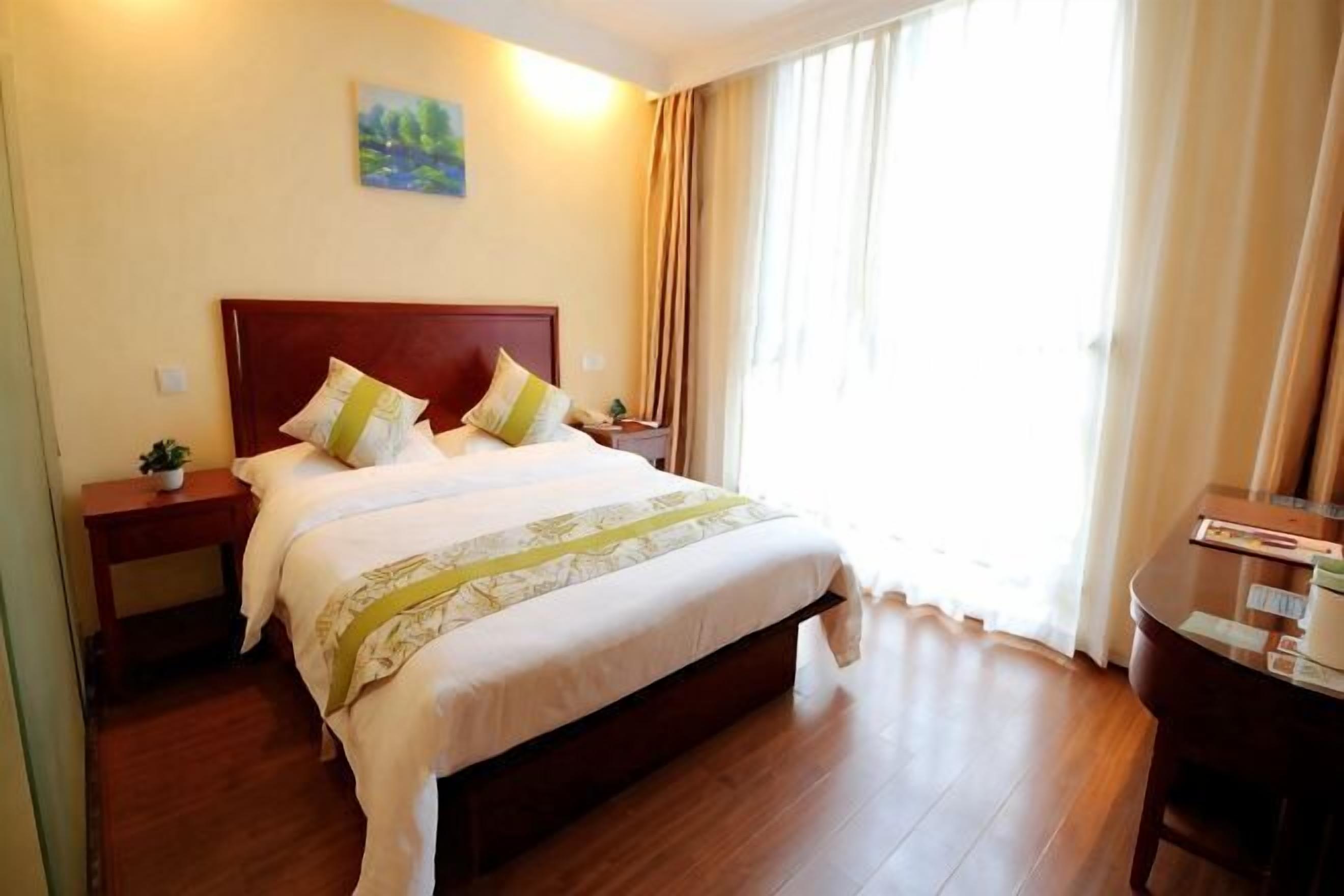 A hotel room with a bed, bedside tables, a desk, and a window with curtains.