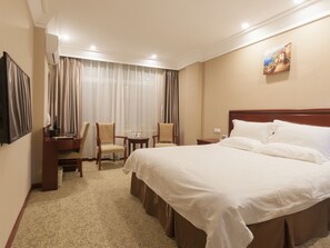 Et hotelværelse med en stor seng, to stole, et skrivebord med lampe og et billede på væggen.