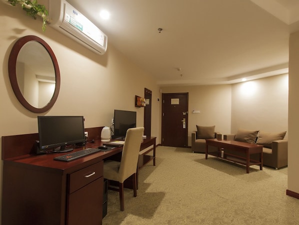 A hotel room with a desk, two chairs, a sofa, a coffee table, a TV, and a mirror.