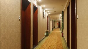 Un couloir d'hôtel avec des revêtements de sol en moquette, des portes en bois et une poubelle verte.