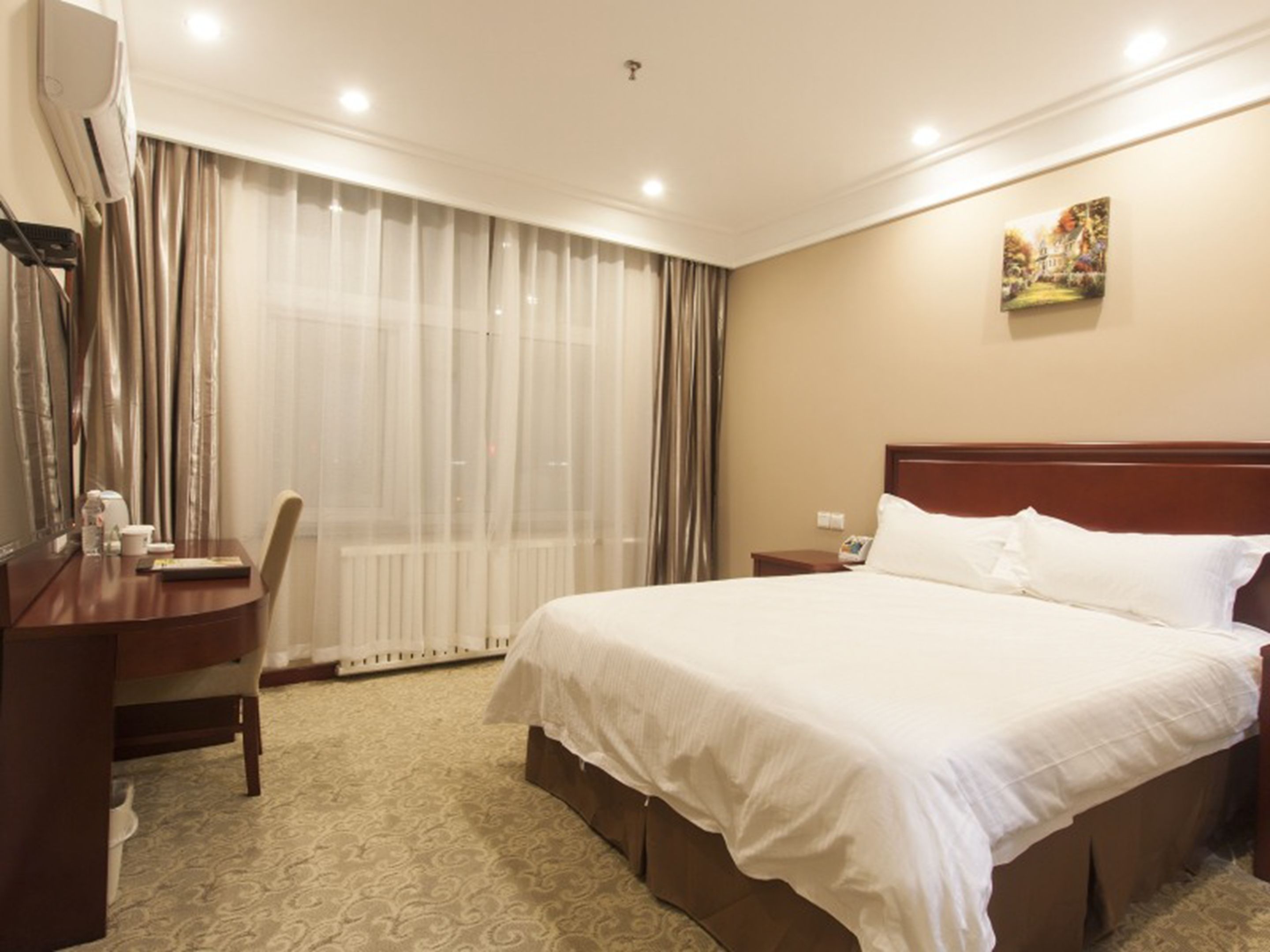 Habitación de hotel con una cama grande, un escritorio de madera, una silla, un radiador y una ventana con cortinas.