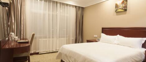 Habitación de hotel con una cama grande, un escritorio de madera, una silla, un radiador y una ventana con cortinas.
