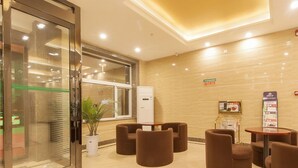 Un hall d’entrée avec une porte vitrée, un comptoir d’accueil, plusieurs coins salons avec des fauteuils marron, et une petite table sur laquelle est posé un présentoir de menus.