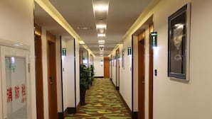 A hotel hallway with patterned carpet, doors, and a potted plant. - Vatica ZaoZhuang TengZhou Railway Station Hotel (Zaozhuang)