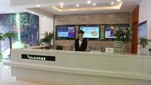 A modern reception desk with digital screens displaying information, a large plant, and a sign indicating a restaurant. - Vatica ZaoZhuang TengZhou Railway Station Hotel (Zaozhuang)