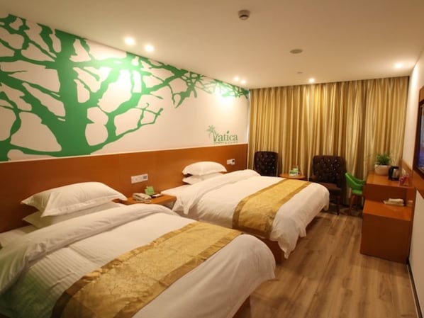 Habitación de hotel con dos camas, un escritorio, una silla, un televisor y una pared decorada con un dibujo de un árbol.