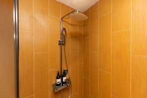 Ducha con cabezal de ducha manual y otro cabezal de lluvia montado en la pared, con dos botellas de champú y acondicionador en un estante debajo.